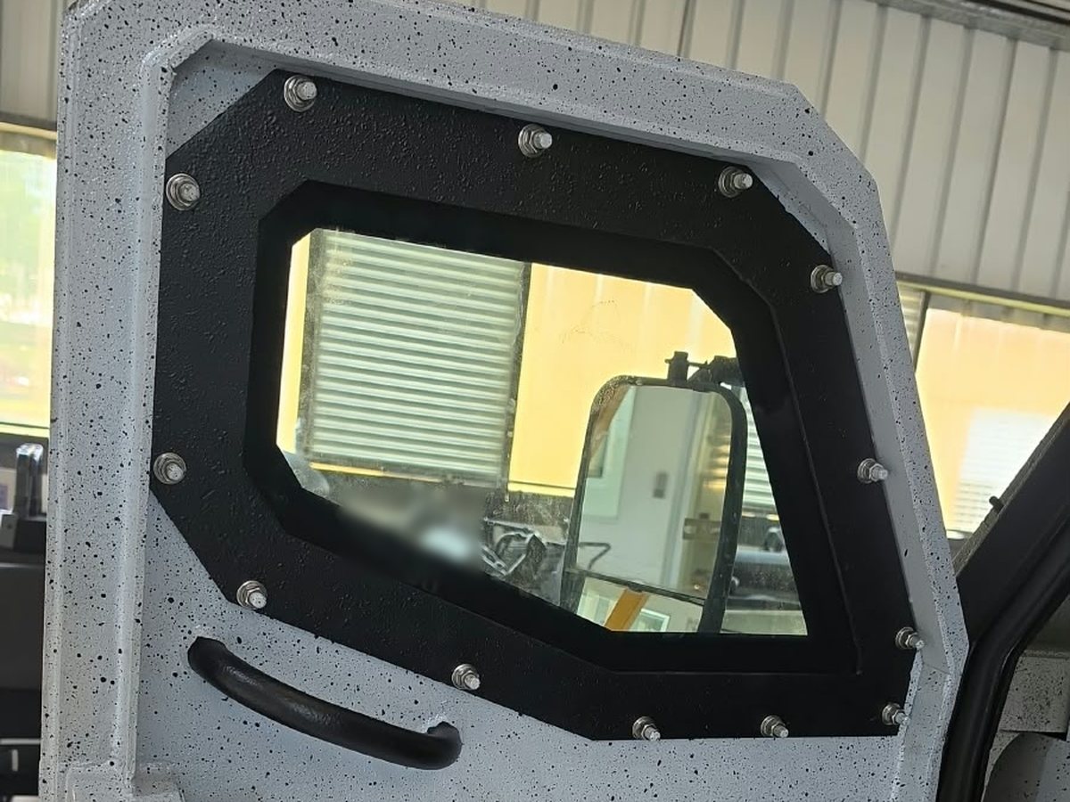 Puerta blindada vista desde dentro, con una ventana de vidrio blindado grueso sujeta con tornillos al marco de acero