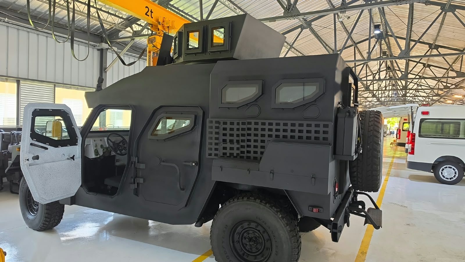 Vehículo blindado compacto con sus dos puertas pesadas abiertas, dentro de una nave industrial